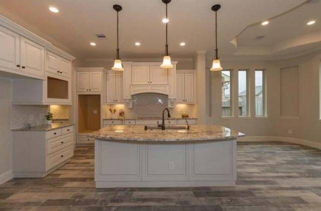 This kitchen features a spacious open layout with a large central island, granite countertops, and elegant pendant lighting. It has ample cabinet space and a stylish tile floor, creating a modern and inviting atmosphere.