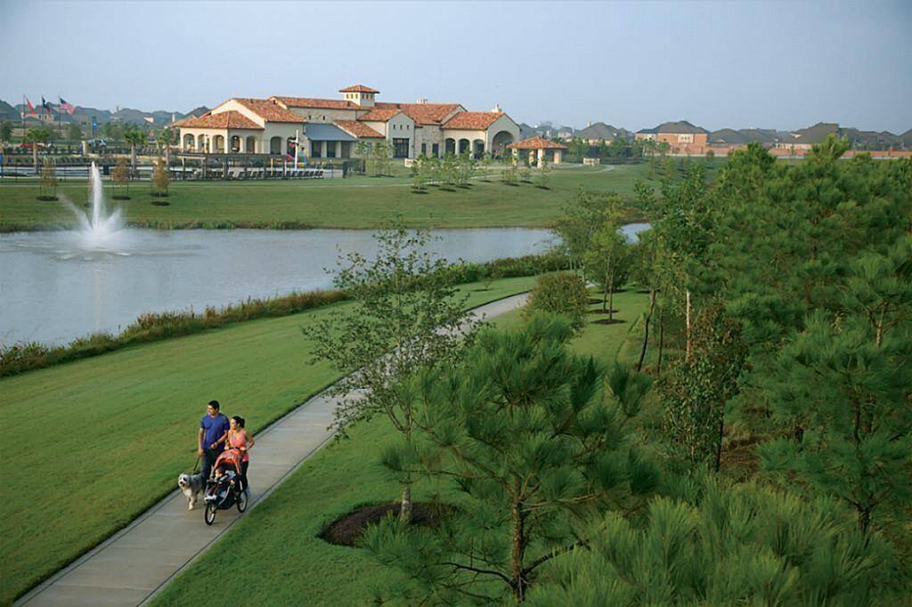 This photo showcases a serene neighborhood with a picturesque landscape. It features a scenic walking path beside a tranquil lake with a fountain, surrounded by lush greenery. The setting suggests a peaceful and family-friendly environment.