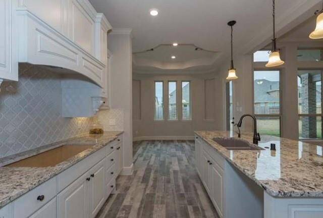 This kitchen features elegant granite countertops, white cabinetry, and modern pendant lighting. The space is complemented by a textured backsplash and wood-look tile flooring, with ample natural light from large windows.