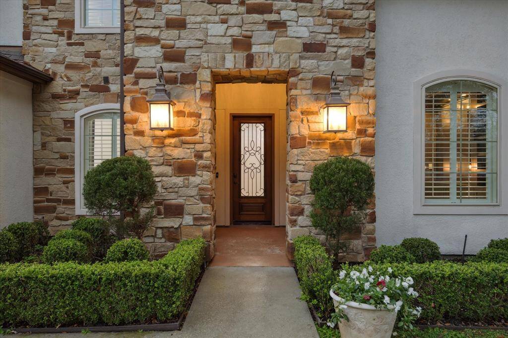 The doorway has a decorative glass insert, flanked by two neatly trimmed hedges and potted plants enhance the welcoming path.