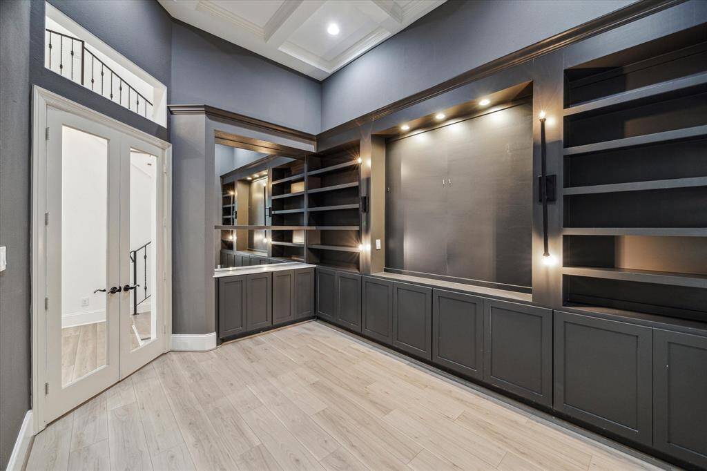 This photo showcases a modern, well-lit room featuring built-in shelving and cabinets, ideal for a home office or library. It has elegant double doors and light vinyl flooring, creating a sophisticated and functional space.
