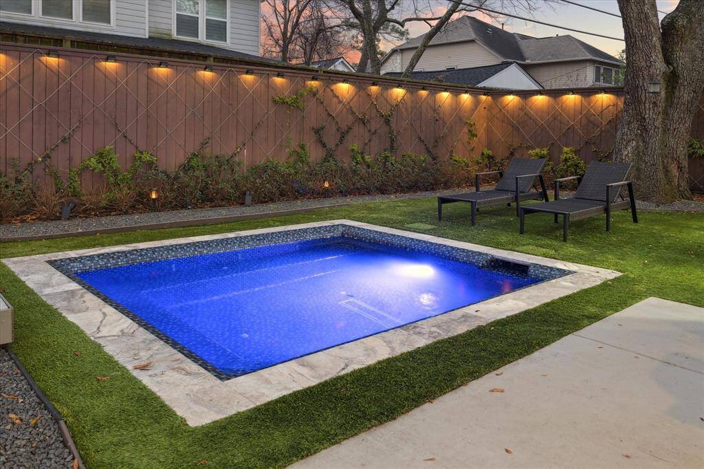 This backyard features a modern, illuminated plunge pool/spa surrounded by lush greenery and turfed lawn, offering a serene and private outdoor retreat.
