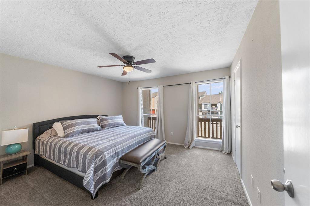 Bright and spacious secondary bedroom featuring a large bed, ceiling fan, and ample natural light from two windows with a view. Neutral tones and cozy carpeting create a welcoming atmosphere.