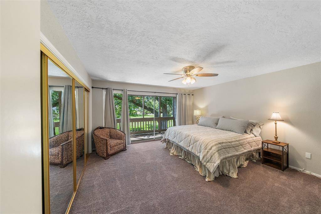 Spacious bedroom with neutral tones, featuring a large bed, mirrored closet doors, and a ceiling fan. The room has ample natural light from sliding glass doors that open to a balcony.