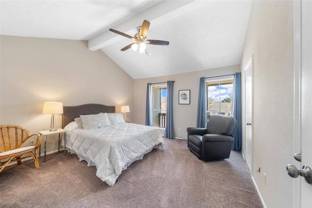 Bright and spacious bedroom with vaulted ceilings, featuring a ceiling fan, large windows for natural light, and cozy carpeting.