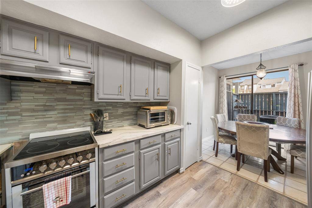Updated kitchen with gray cabinetry, a sleek electric stove, and a stylish tile backsplash. Adjacent is a breakfast area with view of front patio via sliding glass door offering ample natural light.