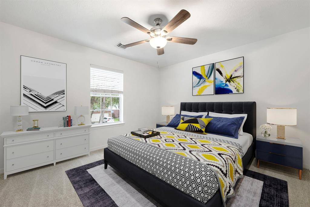 Secondary bedroom features plush carpet, fresh neutral paint, dark stained ceiling fan with lighting and a large window with privacy blinds.