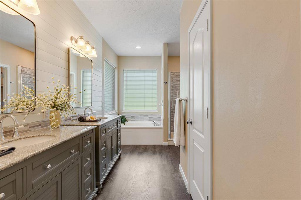 The remodeled bath offers two sinks with their own vanity, up against a shiplap wall, updated lighting, and luxury vinyl flooring