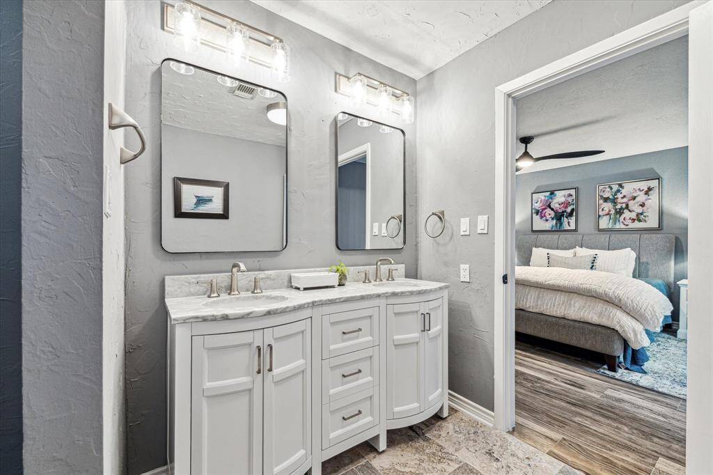 The ensuite bathroom has been beautifully renovated with tile flooring, fresh paint, a furniture-style dual sink vanity with mirrors and vanity lights above, and a fully tiled walk-in shower.