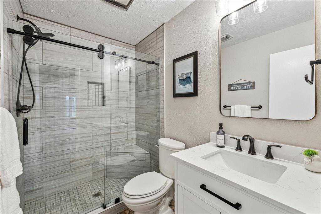 This full guest bathroom is beautifully updated with a modern vanity, mirror and vanity lights above, and a gorgeous fully tiled walk-in shower with upgraded fixtures and frameless glass.