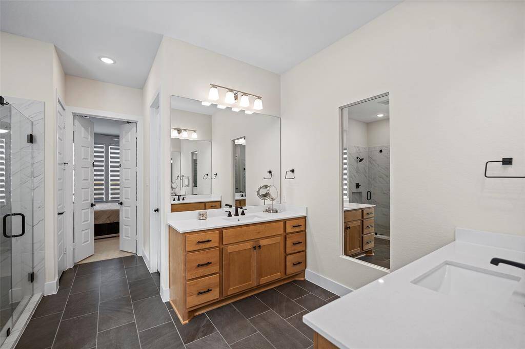 The primary bathroom features dual vanities with ample storage, modern matte black fixtures, and a sleek quartz countertop finish. A spacious walk-in shower with contrasting tile adds to the clean, contemporary feel.