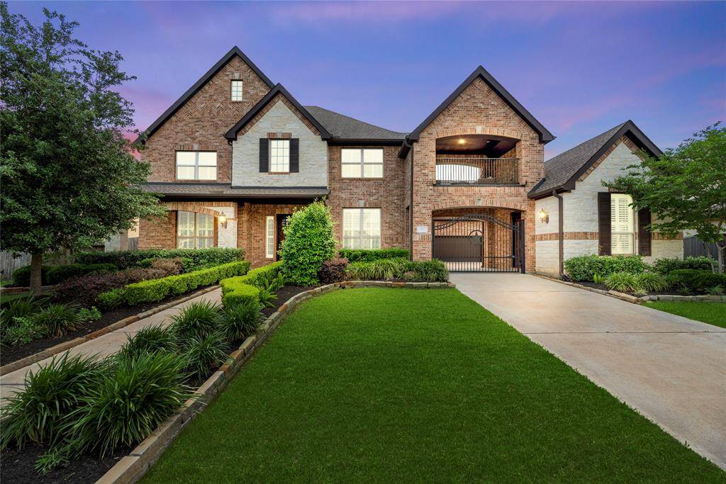 This stunning two-story brick home features a well-manicured lawn, elegant landscaping, and a spacious driveway. The facade offers a welcoming blend of stone and brick elements, with stylish windows and a charming front porch.