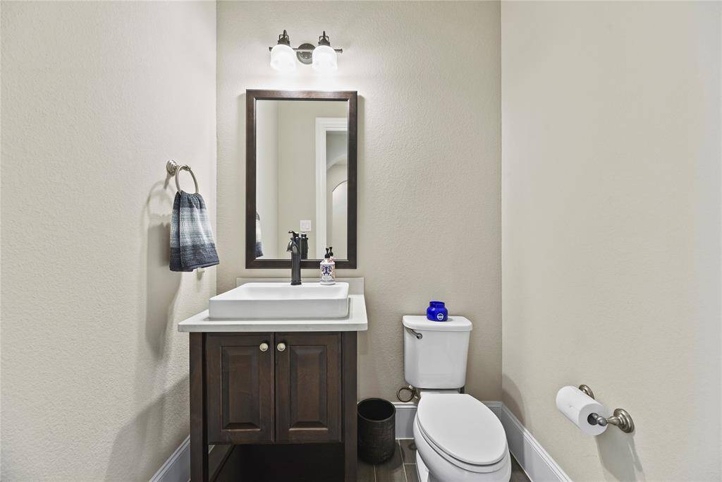 This photo shows a compact, well-lit half-bathroom featuring a modern vanity with a rectangular sink, a wall-mounted mirror, and a toilet. The neutral color scheme and simple decor create a clean and inviting space.