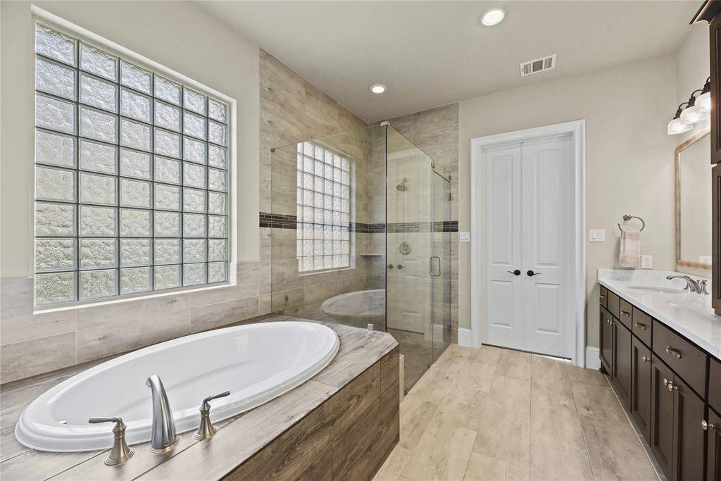 This bathroom features a spacious design with a large soaking tub and a glass-enclosed shower. It boasts elegant tile work, a double vanity with ample storage, and a privacy window, creating a bright and inviting atmosphere.