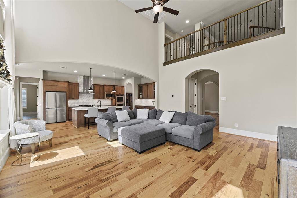 This spacious living area features high ceilings, abundant natural light, and an open floor plan. The kitchen boasts modern appliances and a large island with seating. A cozy sectional and elegant flooring complete the inviting atmosphere.