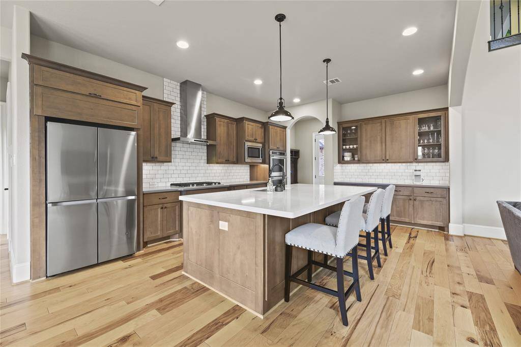 This spacious kitchen features modern stainless steel appliances, a large island with seating, and stylish wooden cabinetry. The light hardwood floors and subway tile backsplash add a bright, contemporary touch.