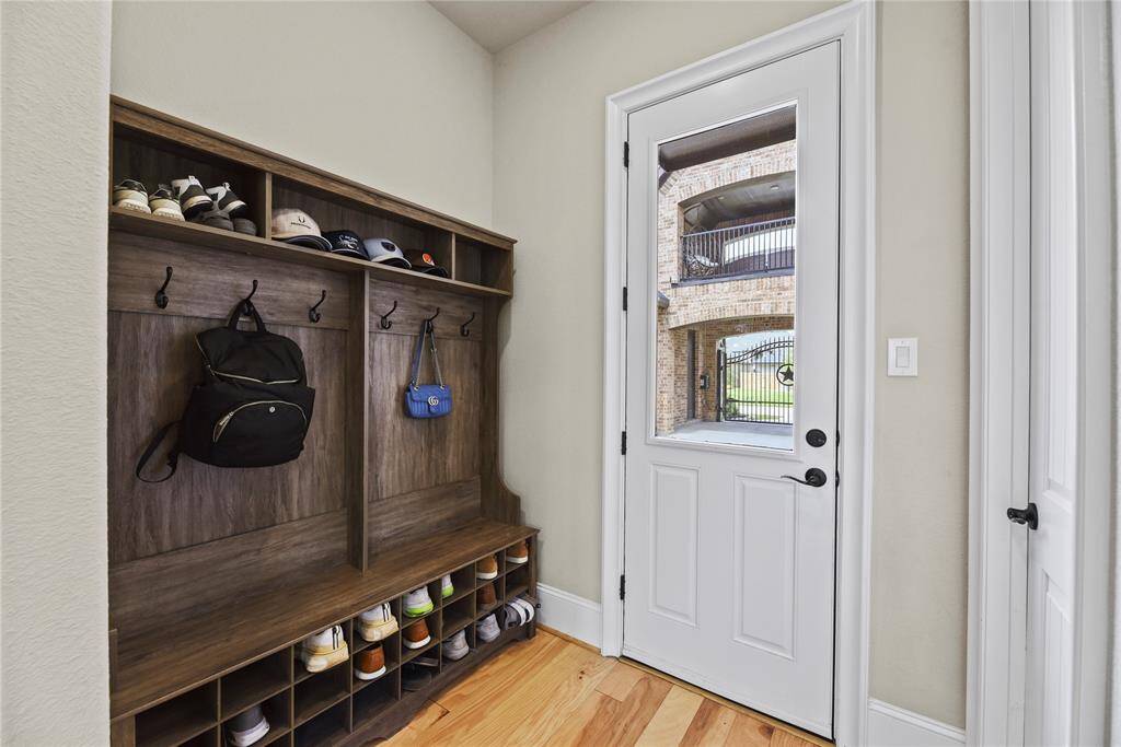 This entryway features a built-in wooden mudroom bench with cubbies and hooks for storage, leading to a door with a window overlooking an outdoor area.