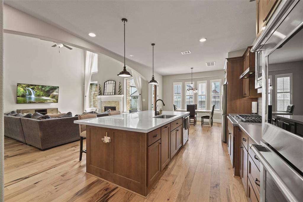 This open-concept home features a spacious kitchen with a large island, stainless steel appliances, and hardwood flooring. The living area, visible from the kitchen, boasts a cozy fireplace and ample natural light from tall windows, creating a welcoming and bright atmosphere.