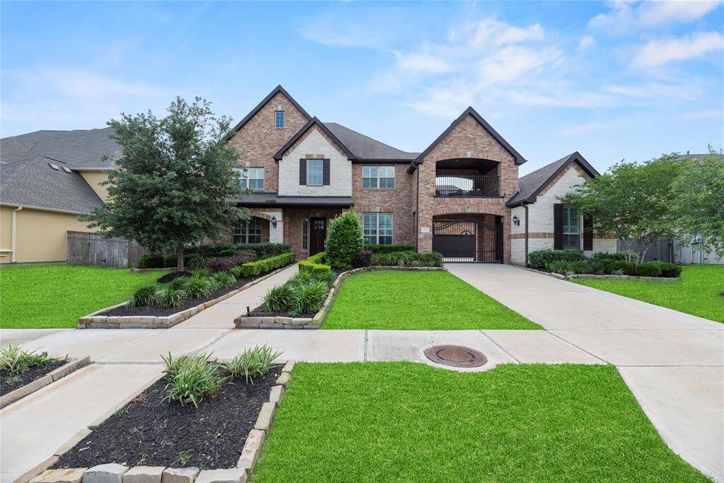 This photo showcases a spacious, two-story brick home with a well-maintained front yard, featuring manicured lawns and landscaped garden beds. The driveway leads to a gated entry, and the house has a welcoming, elegant facade.