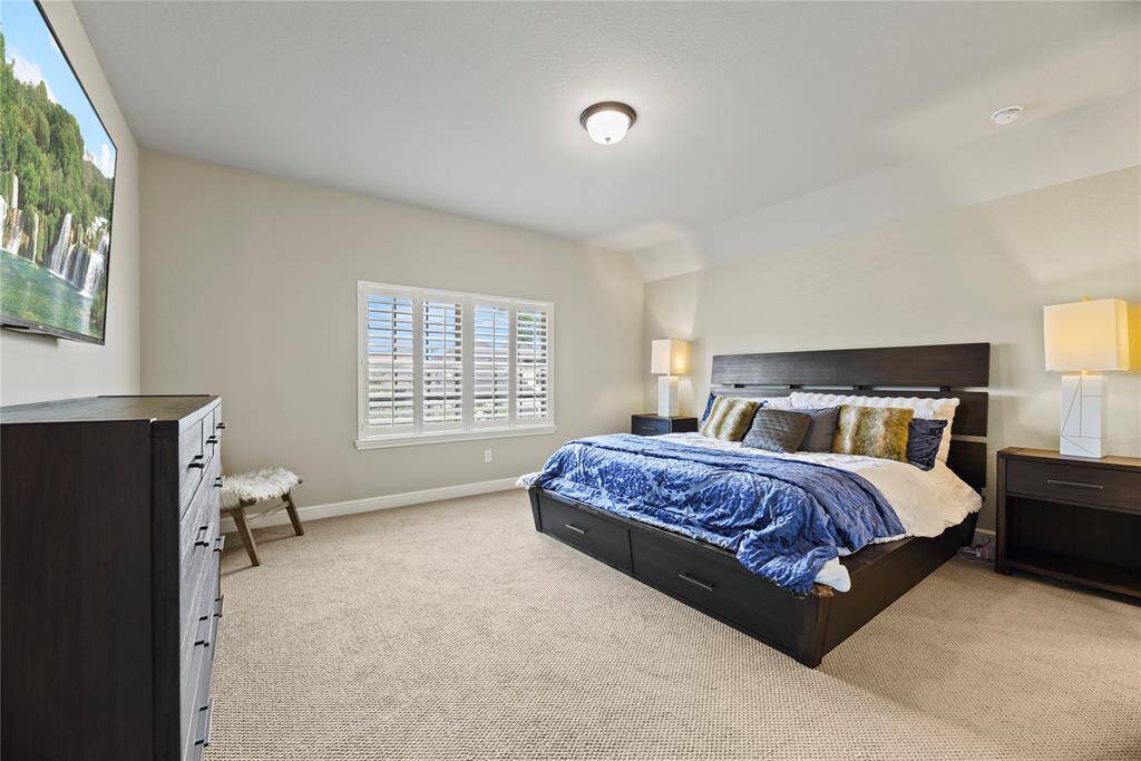Spacious bedroom with neutral tones, featuring a large bed, carpeted floor, and ample natural light from the window. Includes modern furniture and a calming artwork piece, creating a cozy and inviting atmosphere.