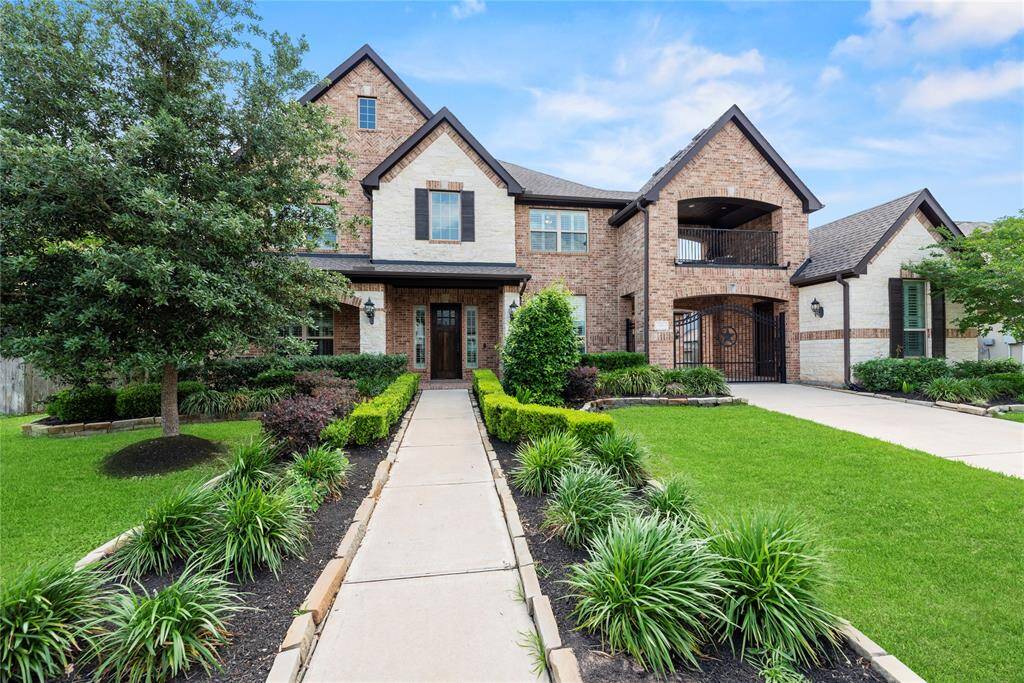 This charming two-story brick home features a beautifully landscaped front yard with a walkway leading to an inviting entrance. It showcases a mix of brick and stone facade, a covered balcony, and a spacious driveway, ideal for family living.