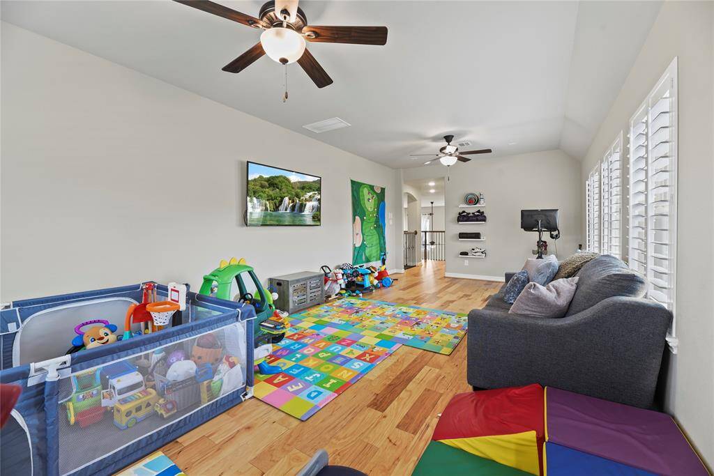 This spacious playroom features hardwood floors, large windows with shutters, and ceiling fans for comfort. It includes a cozy seating area and ample space for toys and activities, making it ideal for children and family fun.