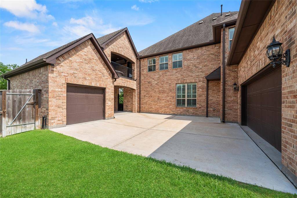 This photo shows a spacious brick home with a large driveway and two garages, featuring a well-maintained lawn and classic exterior lighting.