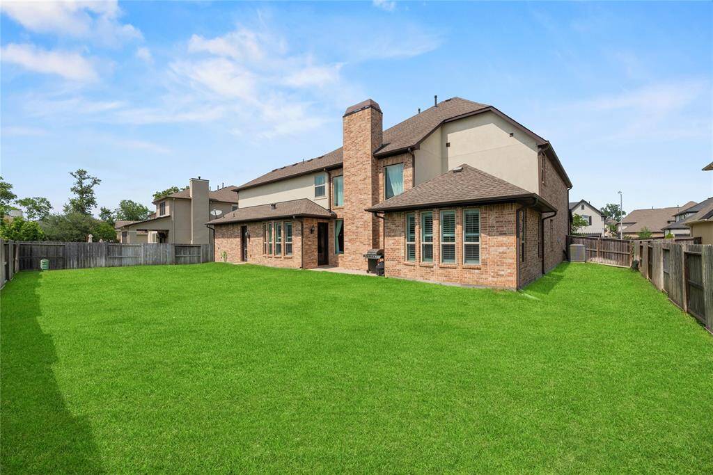 This is a spacious two-story brick home with a large, well-maintained fenced backyard, perfect for outdoor activities. The property features multiple windows for natural light and a charming patio area.