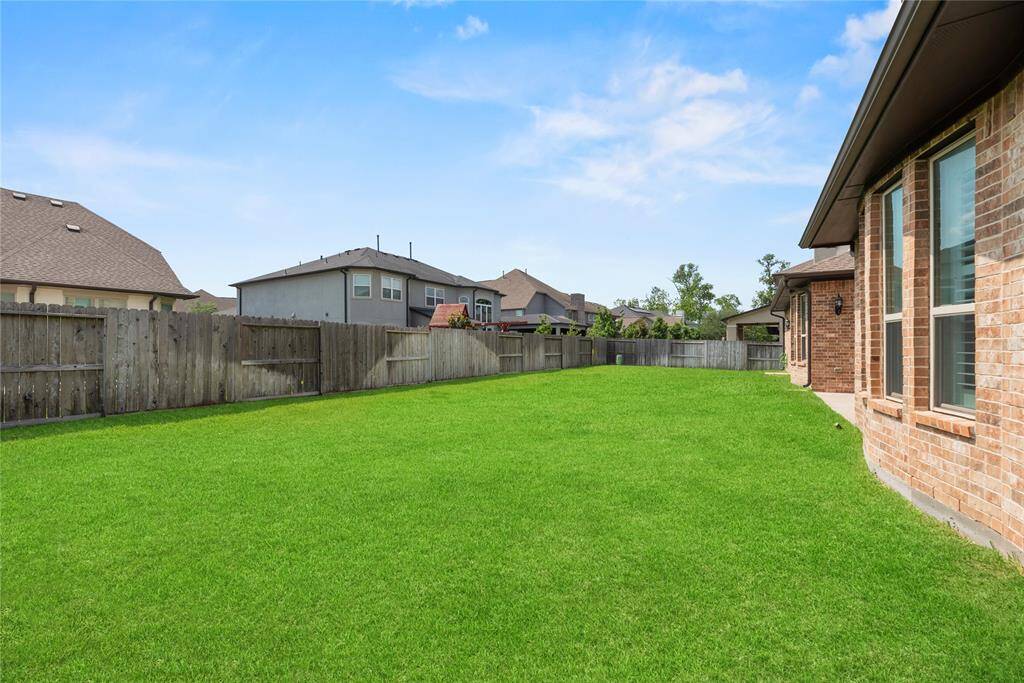 Spacious backyard with a well-maintained lawn, surrounded by a wooden fence for privacy. Neighboring homes are visible, providing a suburban feel. Ideal for outdoor activities or gardening.