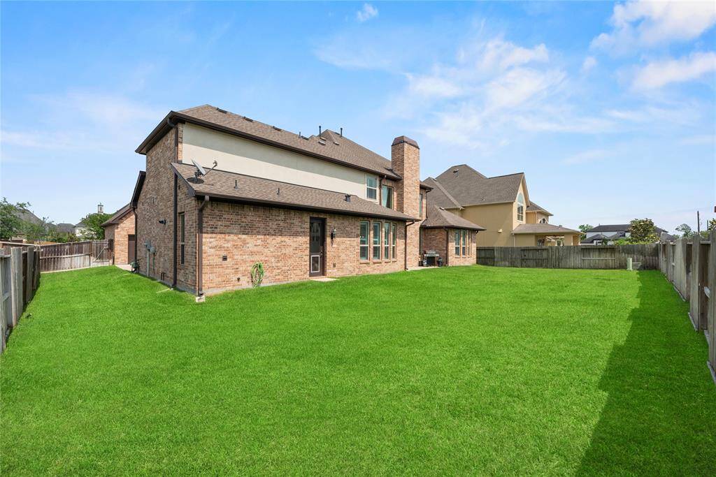 This photo showcases the rear view of a spacious two-story brick home with a large, well-maintained lawn, ample windows, and a central chimney. The setting sun casts a warm glow, highlighting the inviting backyard space.