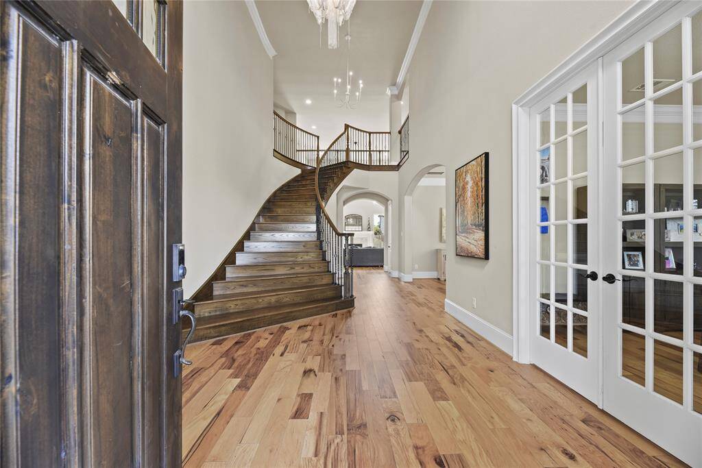 This inviting entryway features a grand wooden staircase, high ceilings, and elegant French doors leading to a bright and spacious living area, creating a warm and welcoming atmosphere.