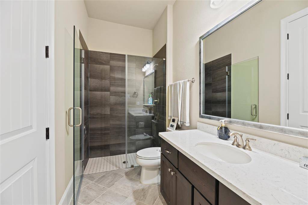 This bathroom features a modern design with a glass-enclosed shower, dark wood cabinetry, and a light marble countertop. The space is complemented by a large mirror and neutral tile flooring, offering a clean and elegant look.