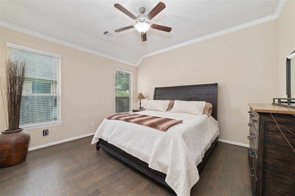 Large primary bedroom again with crown molding high ceilings and wood flooring.