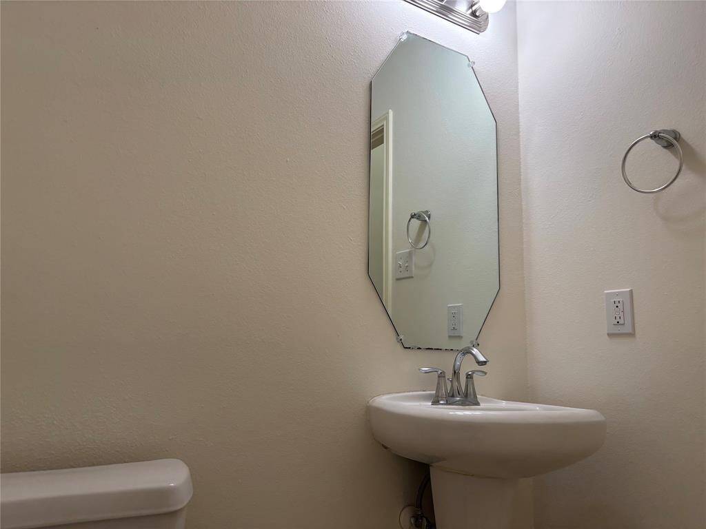 Cozy Half bathroom with a pedestal sink, hexagonal mirror, and modern lighting. Simple and functional design.