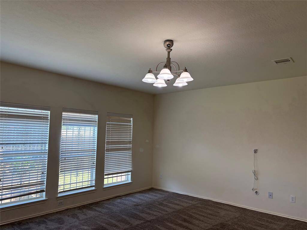 Bright Family room with large windows and blinds, featuring a carpeted floor. There's a ceiling light fixture and wall outlets, ideal for a cozy living space or home office.