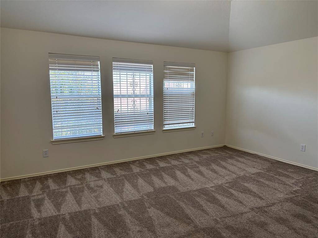 This photo showcases a bright, carpeted family room downstairs. This spacious room features three large windows with blinds, allowing natural light to fill the space. It has neutral-color walls and plush carpet flooring, creating a cozy and inviting atmosphere.