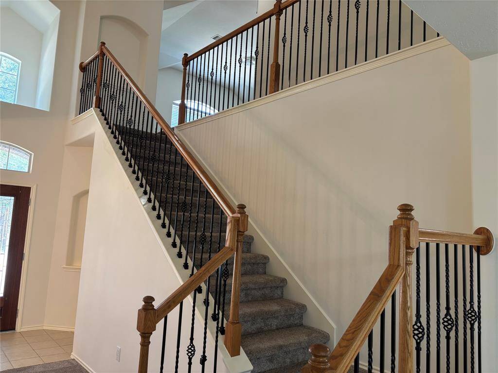 This photo showcases a spacious and elegant staircase with wooden handrails and decorative black metal balusters. The area is well-lit with natural light from nearby windows, creating a warm and inviting entryway.