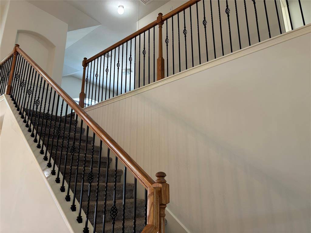 This photo showcases a staircase with elegant dark iron balusters and wooden handrails, leading to an upper floor. The walls are painted in a light neutral tone, enhancing the spacious feel of the area.