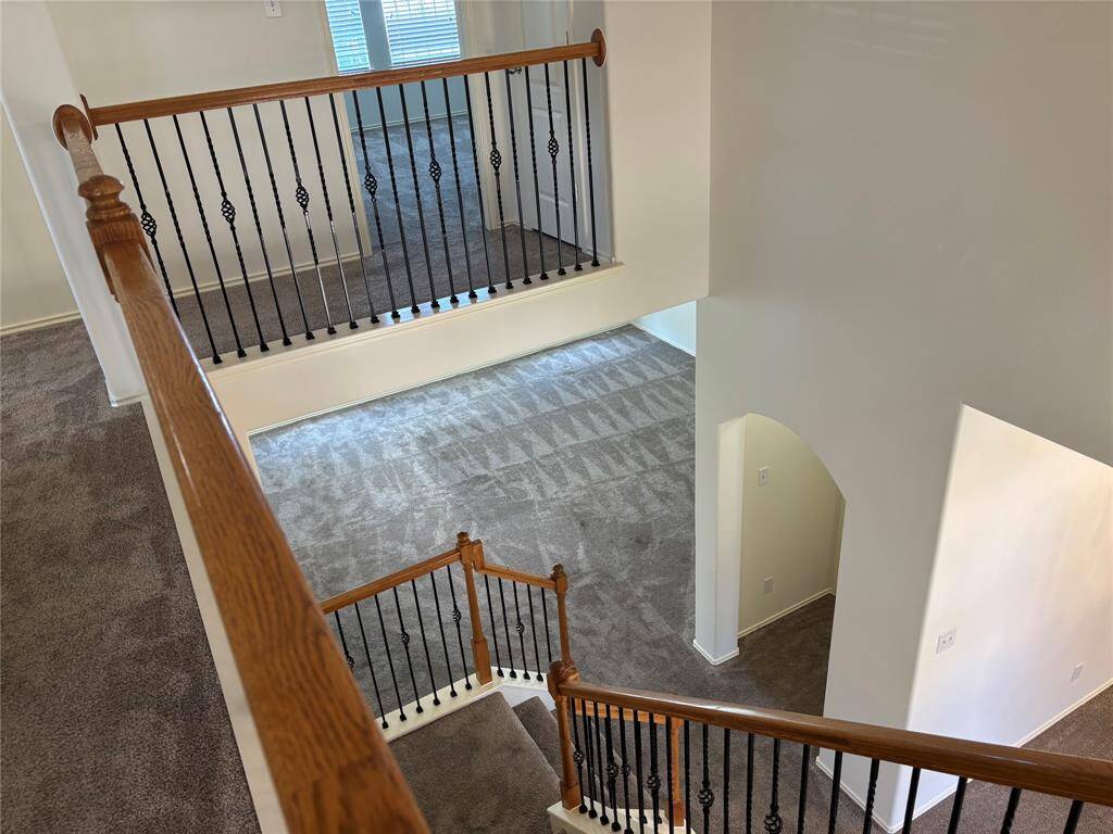 This photo showcases a spacious, multi-level home interior with a staircase featuring wooden handrails and decorative iron balusters. The area is carpeted, and there's an open view of both upstairs and downstairs spaces, offering a bright and inviting atmosphere.