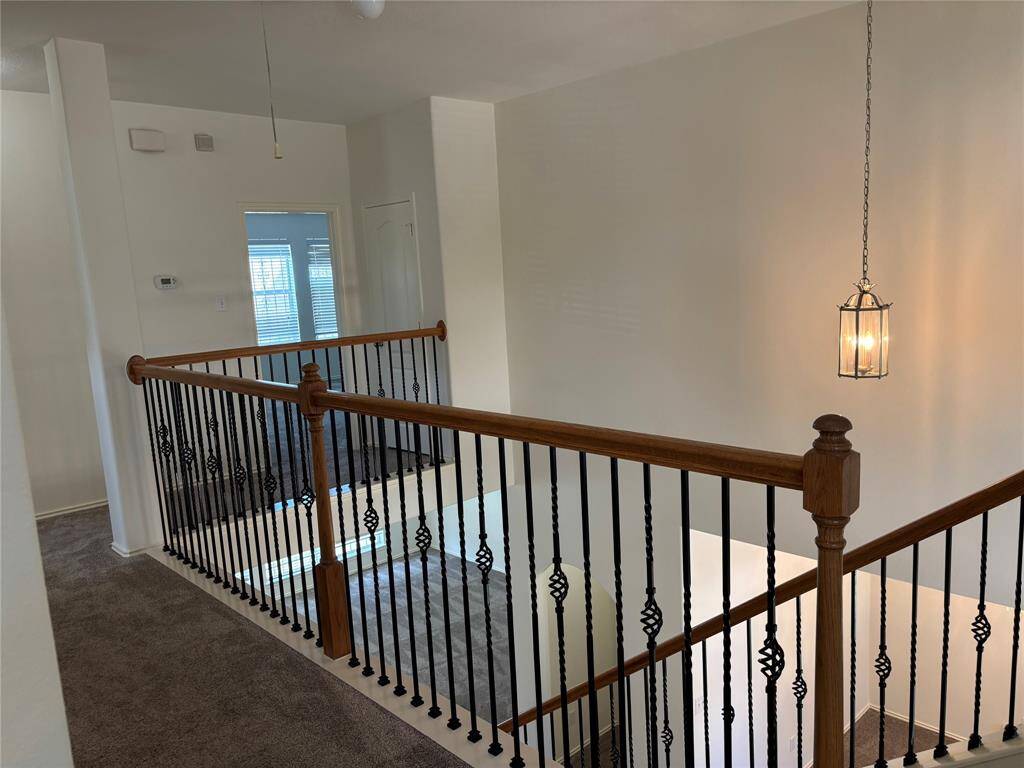 This photo showcases a spacious, multi-level home interior with a staircase featuring wooden handrails and decorative iron balusters. The area is carpeted, and there's an open view of both upstairs and downstairs spaces, offering a bright and inviting atmosphere.