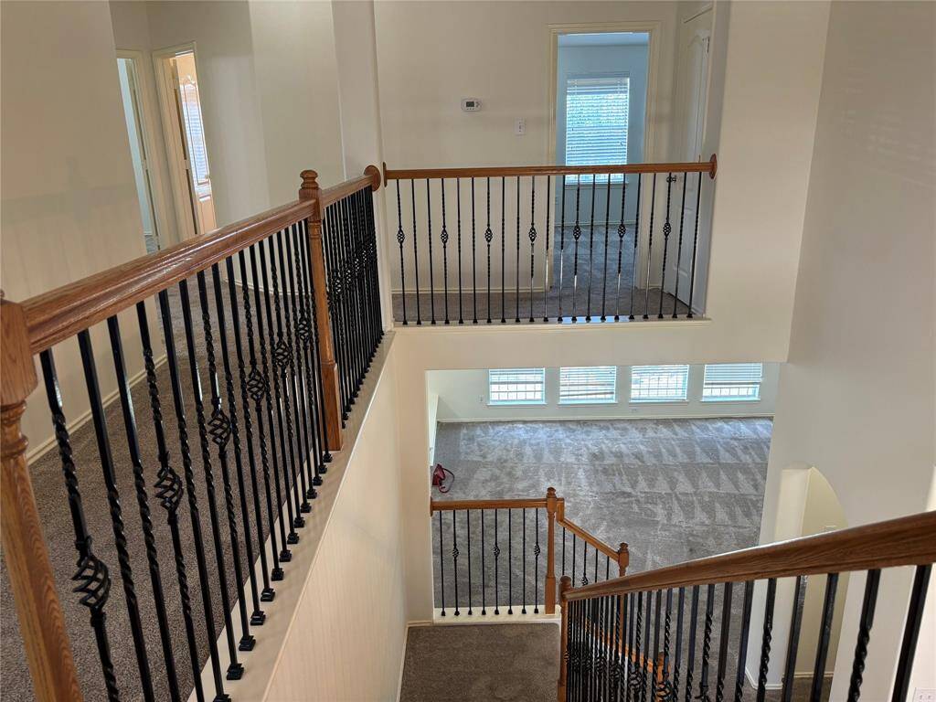 This photo showcases a multi-level interior with carpeted floors, elegant wrought iron and wood railings, and abundant natural light from large windows. The open layout provides a view of both upper and lower levels, offering a spacious and connected feel.