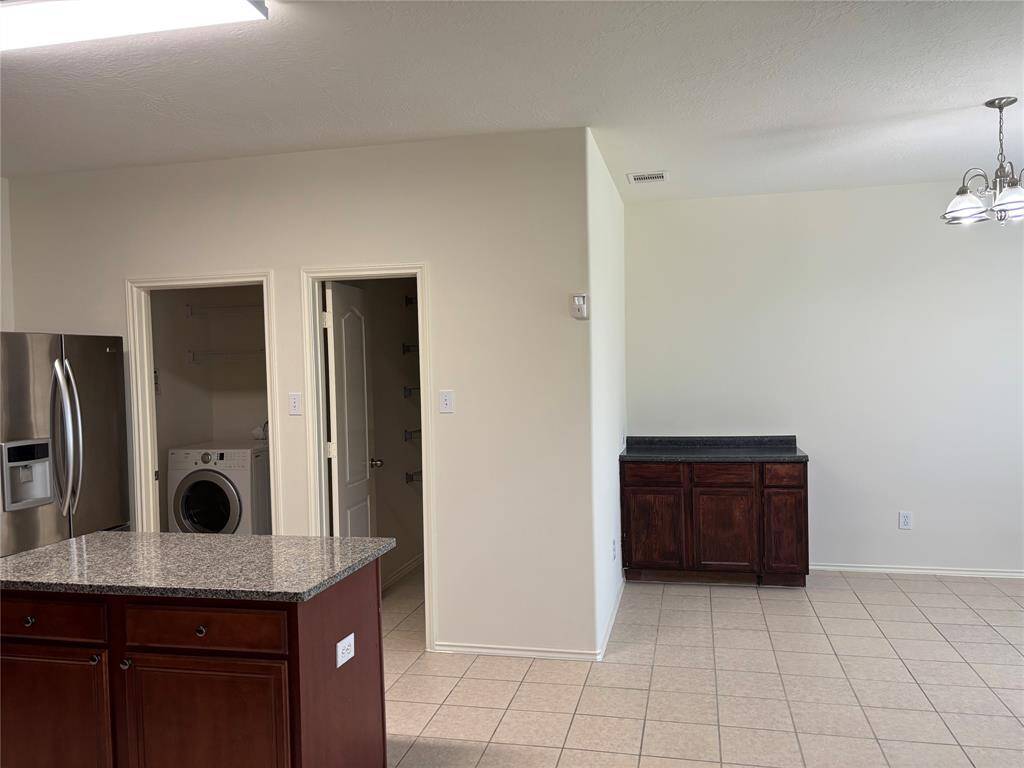 This home features an open layout with a kitchen and dining area, showcasing modern appliances, granite countertops, and tile flooring. The space includes a cozy carpeted section and ample natural light from large windows, creating a welcoming atmosphere.