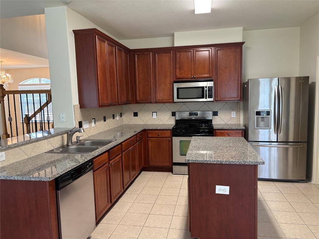 Spacious kitchen with cherry wood cabinets, granite countertops, stainless steel appliances, and a central island. Features a double sink, tile flooring, and a modern backsplash. Bright and open design.