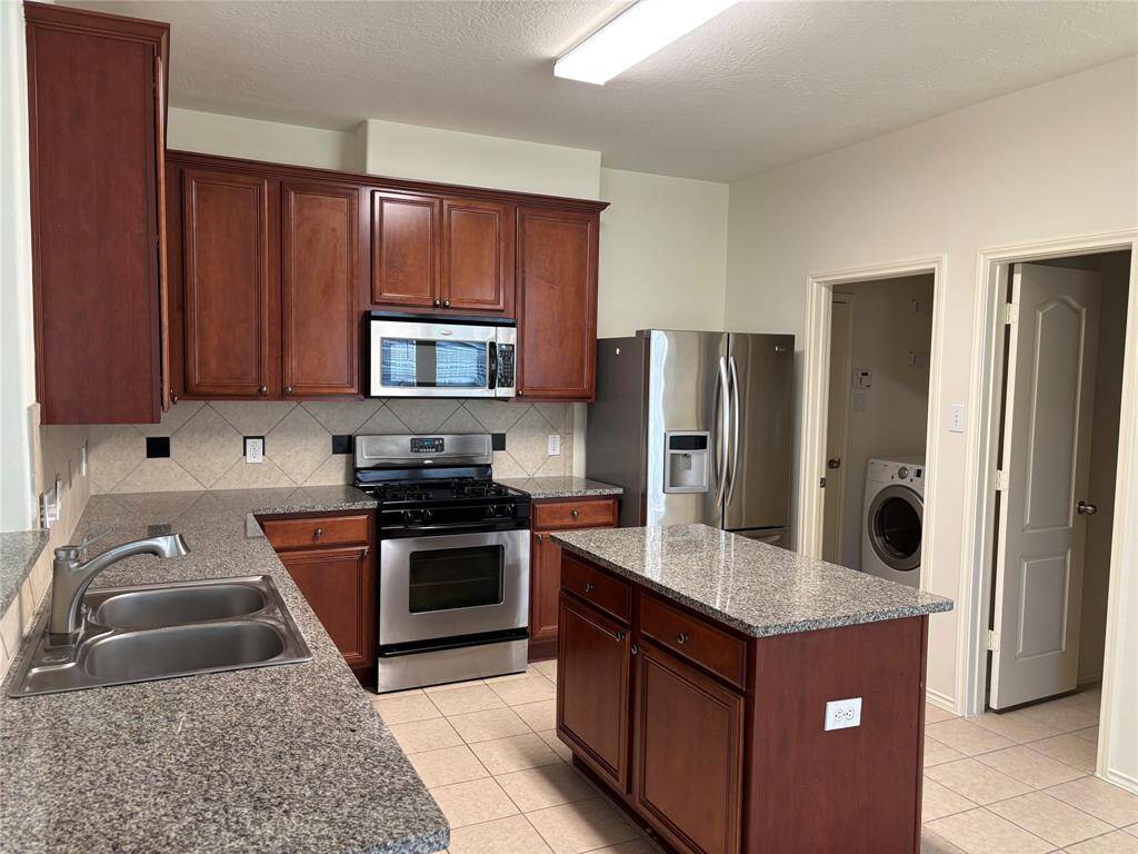 This kitchen features elegant dark wood cabinets, granite countertops, and stainless steel appliances. It includes a central island for extra prep space and opens to a laundry area with modern appliances.