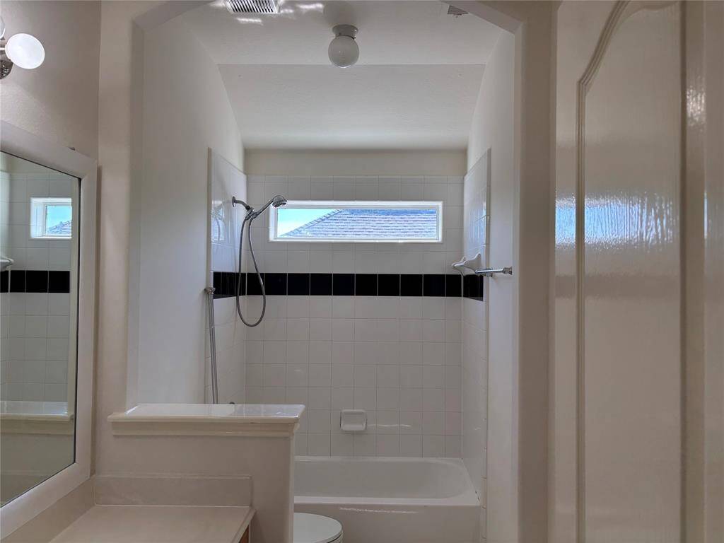 This bathroom features a clean, modern design with a white tiled shower and black accent strip. It includes a window for natural light, a shower-tub combo, and minimalistic fixtures for a sleek look.