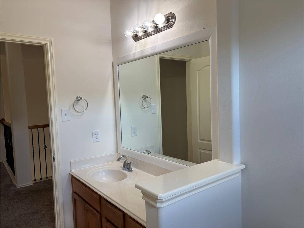 This bathroom features a single sink vanity with a large mirror and overhead lighting. There's a bathtub with tiled surround, and it leads to a walk-in closet with carpet flooring and a window for natural light.