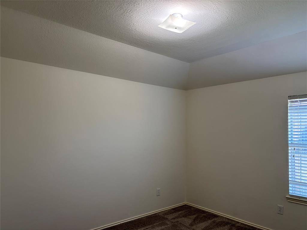 This game room features a vaulted ceiling with a modern light fixture, neutral wall colors, and a door leading to an adjoining space. Natural light filters in through window blinds, creating a bright and airy atmosphere.