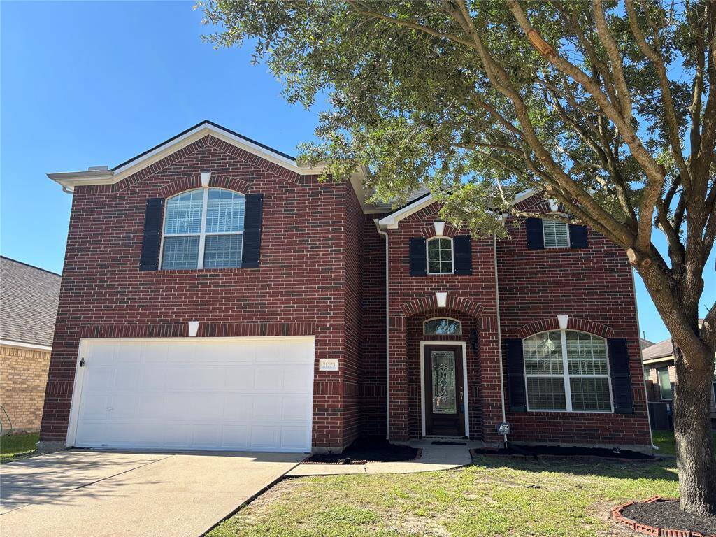 This is a two-story brick home with a classic facade featuring black shutters and arched windows. It has a two-car garage and a front yard with a mature tree providing shade.