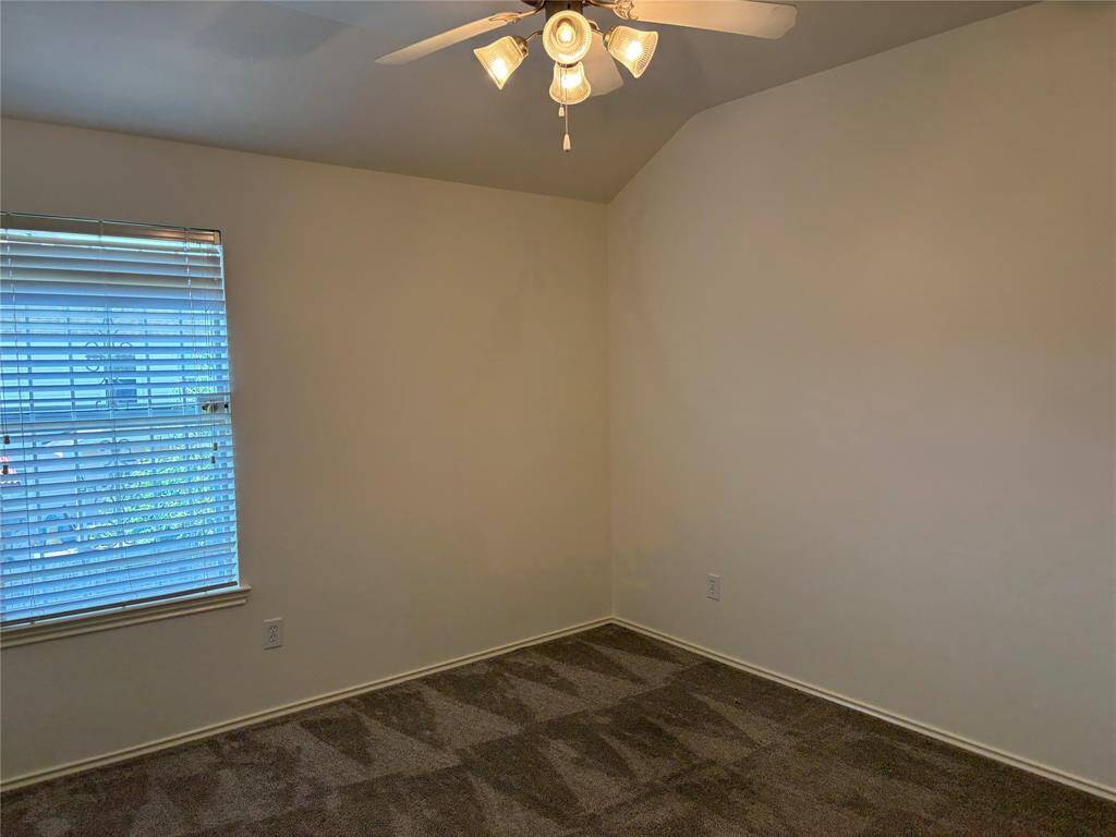 This room features neutral walls, a ceiling fan with lights, carpeted flooring, and a window with blinds, providing a comfortable and versatile space.