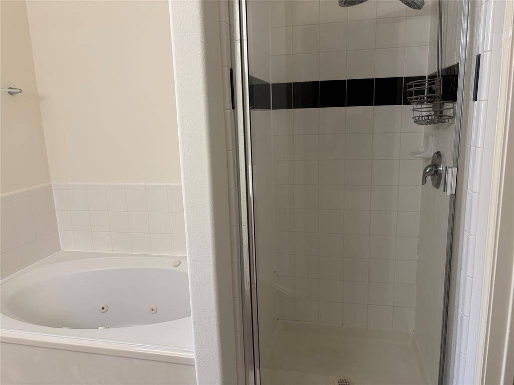 This bathroom features a separate glass-enclosed shower with white and black tile accents, next to a spacious corner bathtub with a tiled surround.